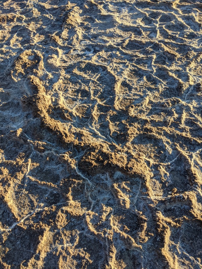 Close up of the ground, showing large brown ridges with veins of white salt ridges between them.