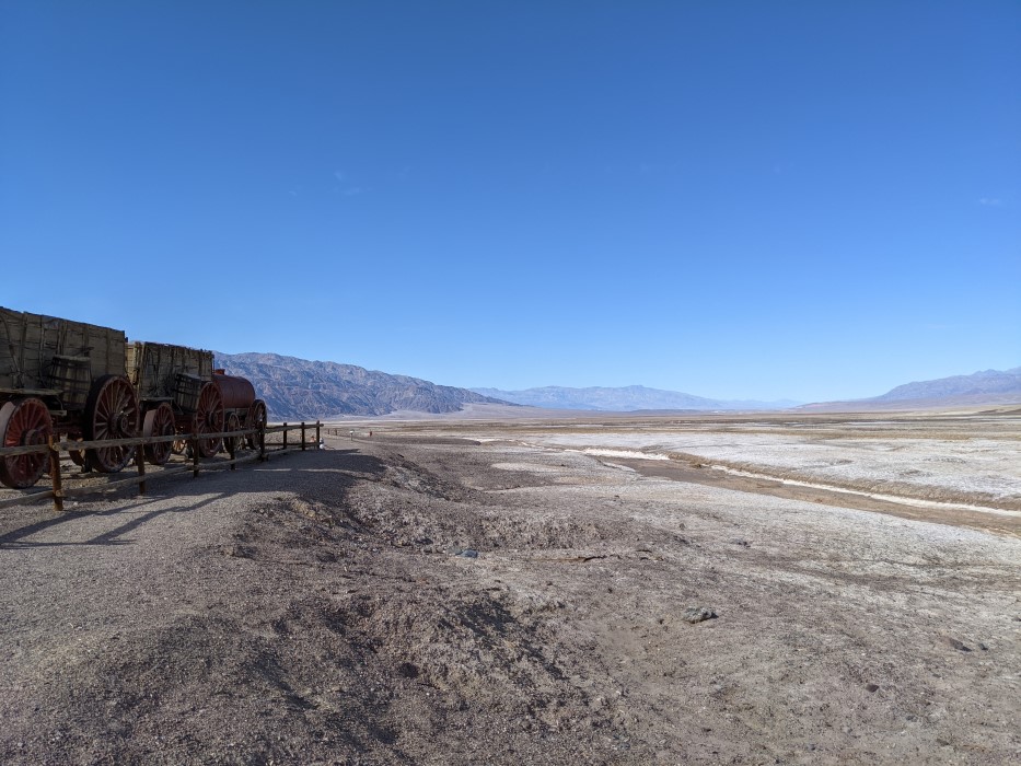 On a slight rise, part of a train of wooden carts with an engine in front can be seen. Below, plains of white stuff stretch out almost to the horizon, with mountains in the background. Still no plants.