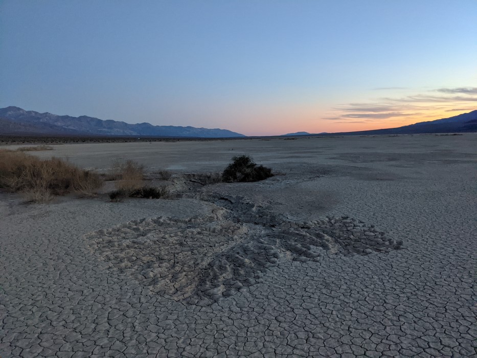 A similar landscape, except indentations in the clay form a rippling fractal-like fan, leading to a deeper indentation which might have been a pond .