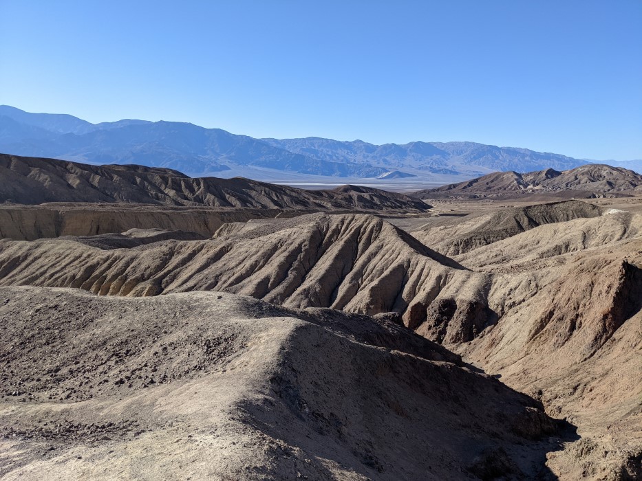 Rolling hills, without vegetation but heavily wrinkled with deep valleys from a past rain. Each hill is only tens of feet across, and they continue into the distance. In the far distance a plain can be seen, and mountains beyond.